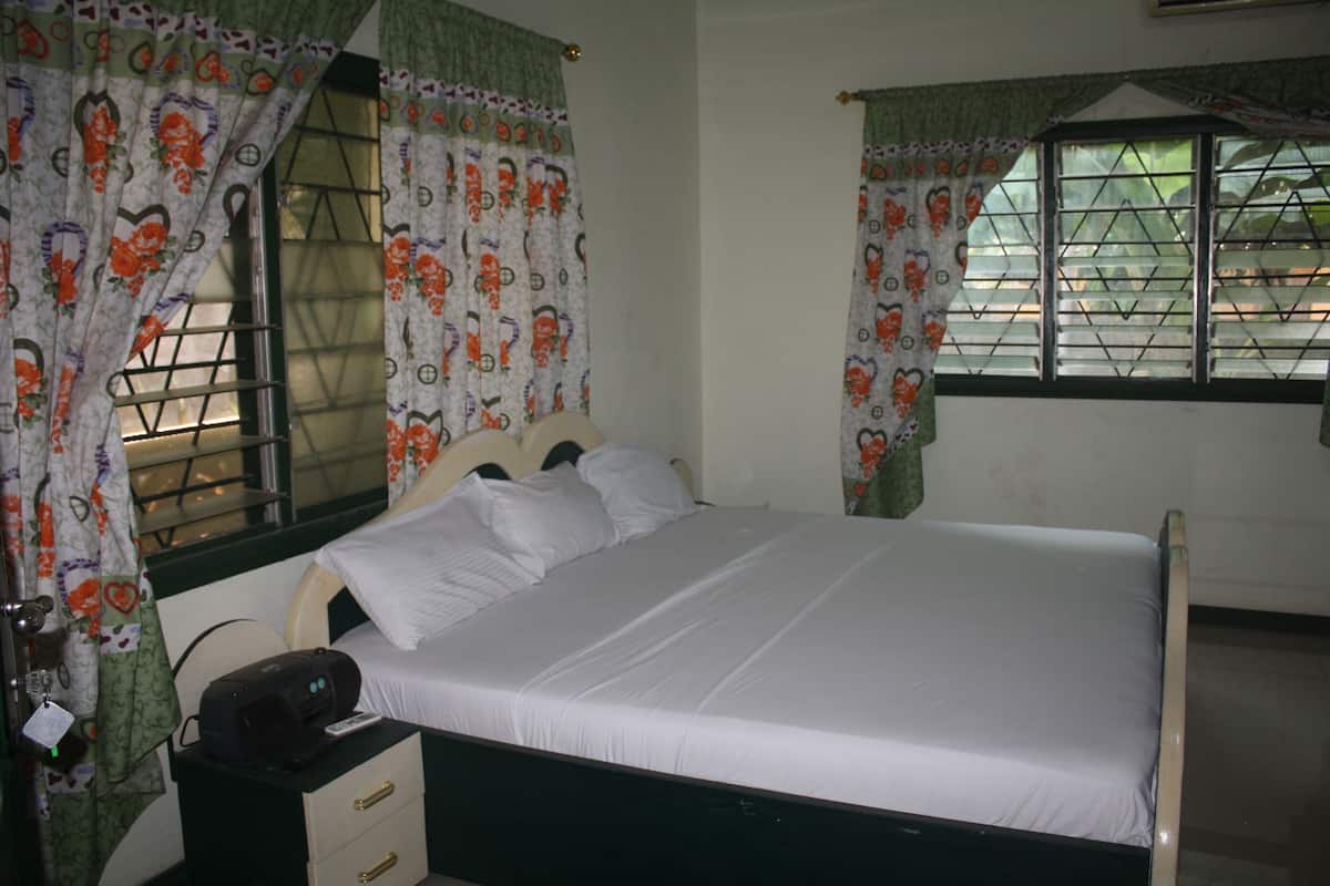 A bedroom with a single bed, a nightstand, a window with bars, and curtains with a floral pattern.