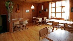 A wooden interior with a dining area, tables, chairs, a hanging guitar, and a window with curtains. - Brekkulækur Guesthouse (Hvammstangi)