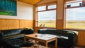 A room with two black leather sofas, a wooden coffee table, and a painting of a forest on the wall. - Brekkulækur Guesthouse (Hvammstangi)