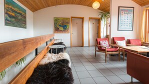 A cozy interior with wooden benches, a dining area with red chairs, and a framed poster on the wall. - Brekkulækur Guesthouse (Hvammstangi)
