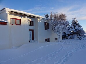 A two-story building with a snow-covered roof and windows. There is a tree with snow on its branches to the right.
