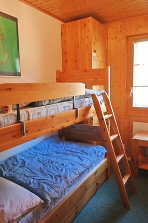 Een slaapkamer met een stapelbed, een ladder, houten wanden en een raam.