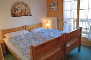 Een houten bed met een kleurrijke deken, een bedlampje, een radiator aan de muur en een raam met gordijnen.