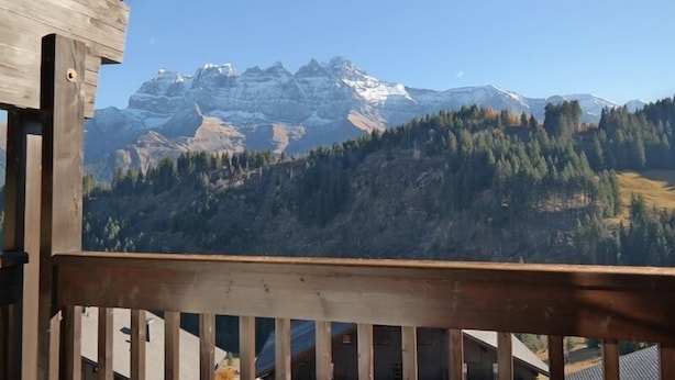 A wooden balcony with a view of snow-capped mountains and a forested valley. - Appartement Myrtilles 25 (Val d'Illiez)