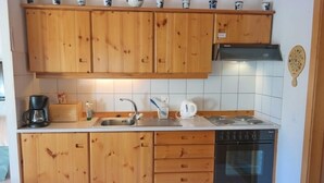 A compact kitchen with wooden cabinets, a built-in stove, a dishwasher, and a coffee maker. - Appartement Myrtilles 25 (Val d'Illiez)
