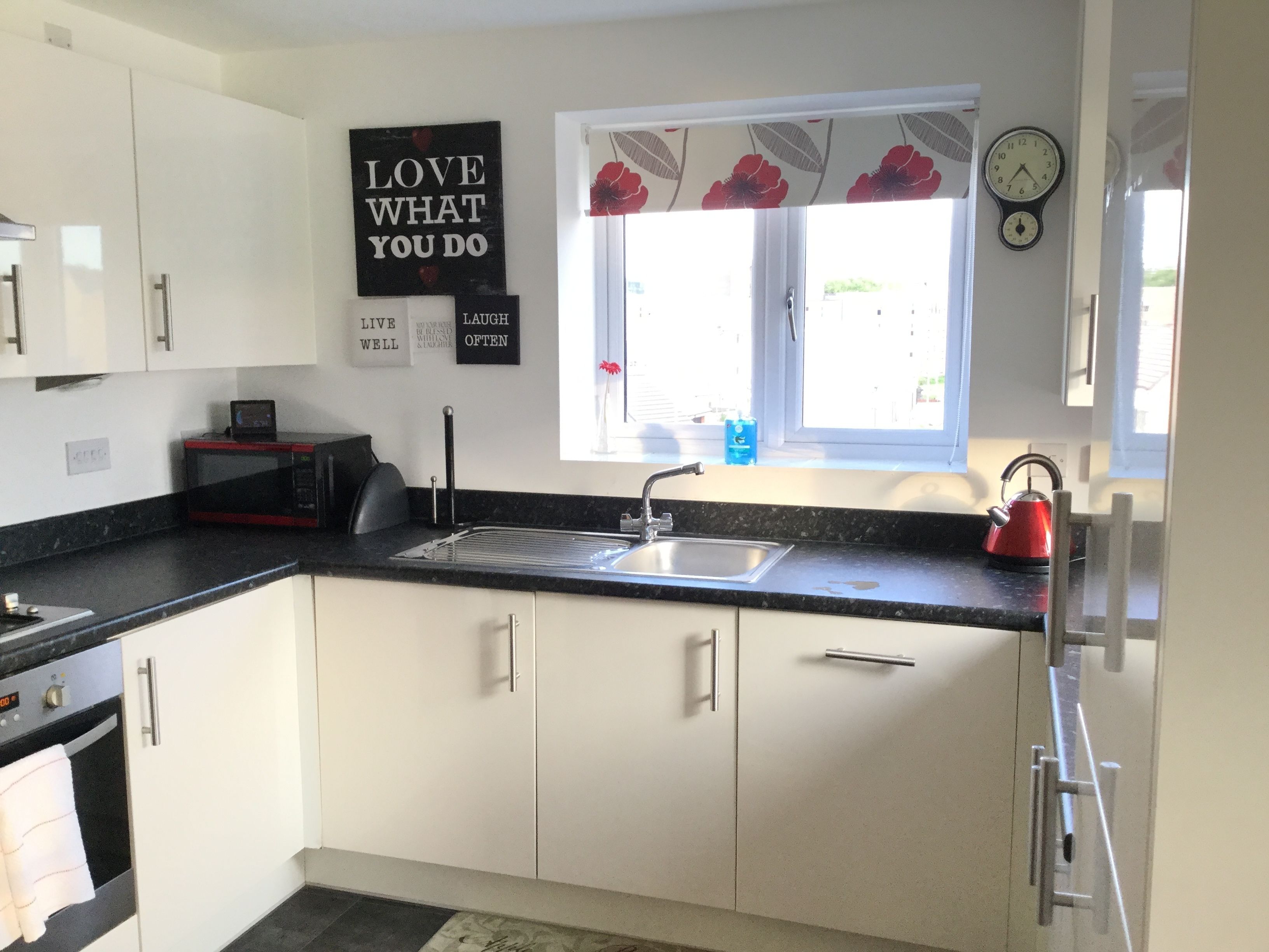A modern kitchen with white cabinets, a black countertop, a sink, a red kettle, and motivational wall art.