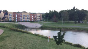 A grassy area with a pond, a small tree, and a building in the background. - Two Bedroom Apartment in Basildon (Basildon)