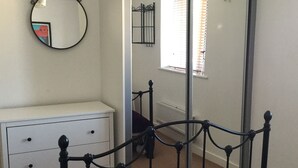 A bedroom with a bed, a dresser, a mirror, and a window with blinds. - Two Bedroom Apartment in Basildon (Basildon)