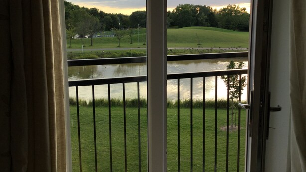 A view from a balcony overlooking a grassy area with a pond and trees. - Two Bedroom Apartment in Basildon (Basildon)