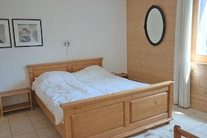 A wooden bed in a room with a white wall, a small wooden nightstand, and a mirror. - Appartement Moilles 13 (Val d'Illiez)