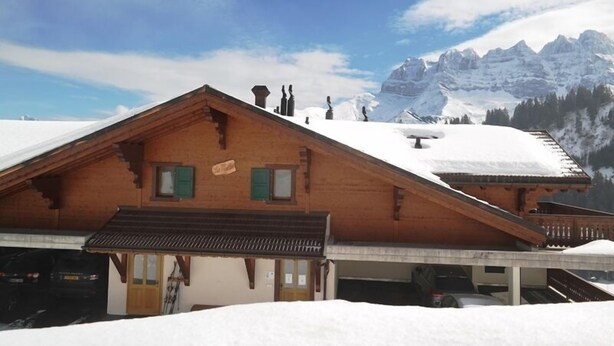 Un chalet en bois avec un toit en pente, un petit porche et une vue sur des montagnes enneigées.