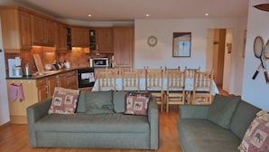 A living room with a sofa, a dining table with chairs, wooden cabinets, a clock, and tennis rackets on the wall. - Appartement Esserts B40 (Val d'Illiez)