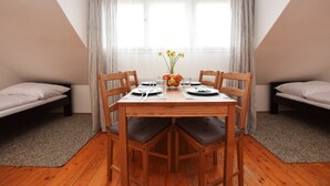 A dining area with a wooden table, six chairs, a vase with flowers, and two beds with pillows. - Císařka apartment (Prague)