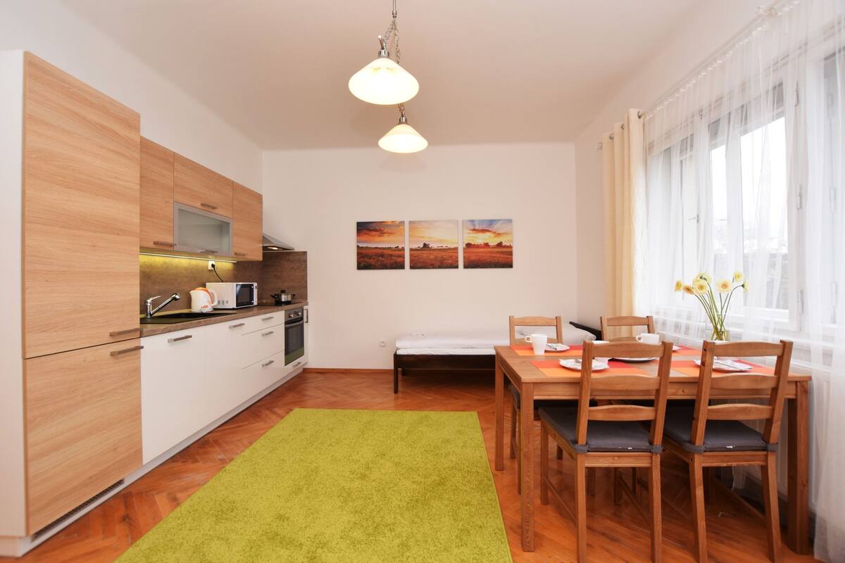 A compact kitchen with modern appliances, a dining area with wooden furniture, and a large window with curtains.
