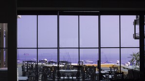 Vue depuis l’intérieur d’un bâtiment doté de grandes fenêtres donnant sur une marina où sont amarrés des bateaux.