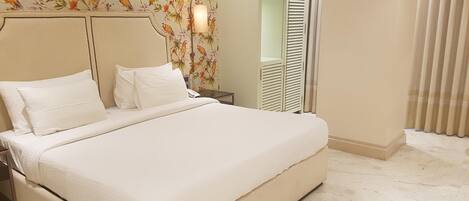 A hotel room with a large bed, a nightstand, a lamp, a wardrobe with louvered doors, and a floral wallpaper.