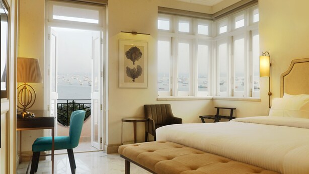 Une chambre d’hôtel avec un grand lit, un bureau avec une lampe, une chaise et une vue sur la mer par la fenêtre.