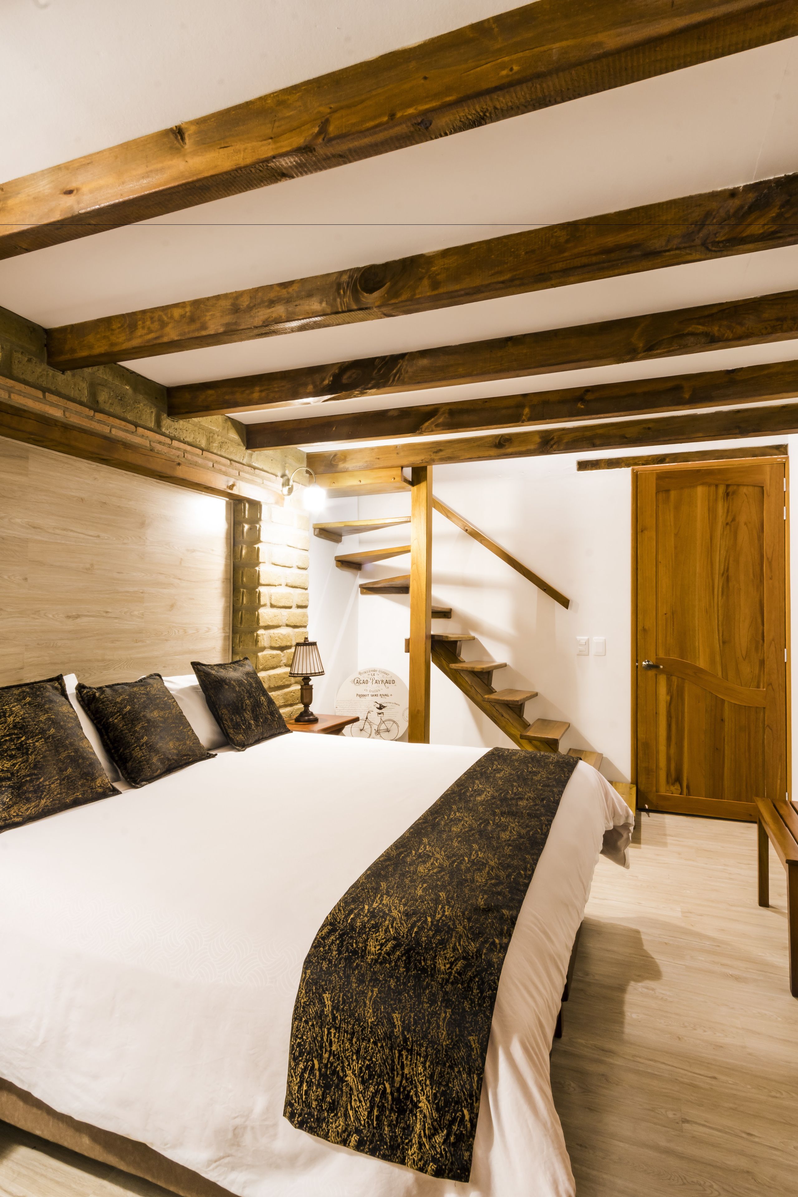 Un dormitorio con una cama grande, vigas de madera, una escalera y una puerta de madera.