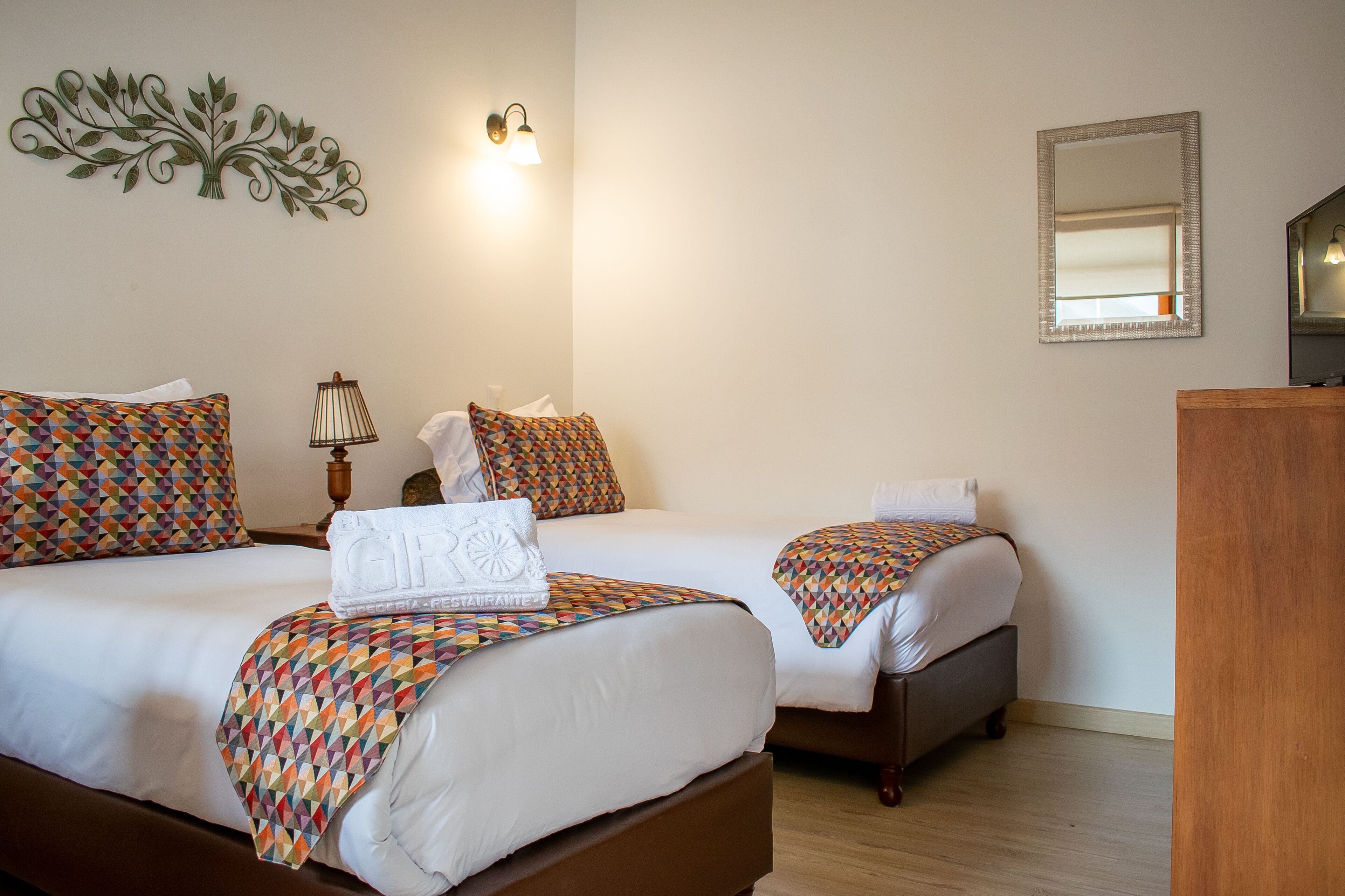 A hotel room with two beds, a wooden dresser, a wall-mounted mirror, and a decorative wall piece.