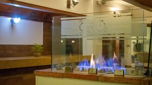 A glass enclosure with a fireplace, featuring a logo and text. - Hotel El Giro (Villa de Leyva)