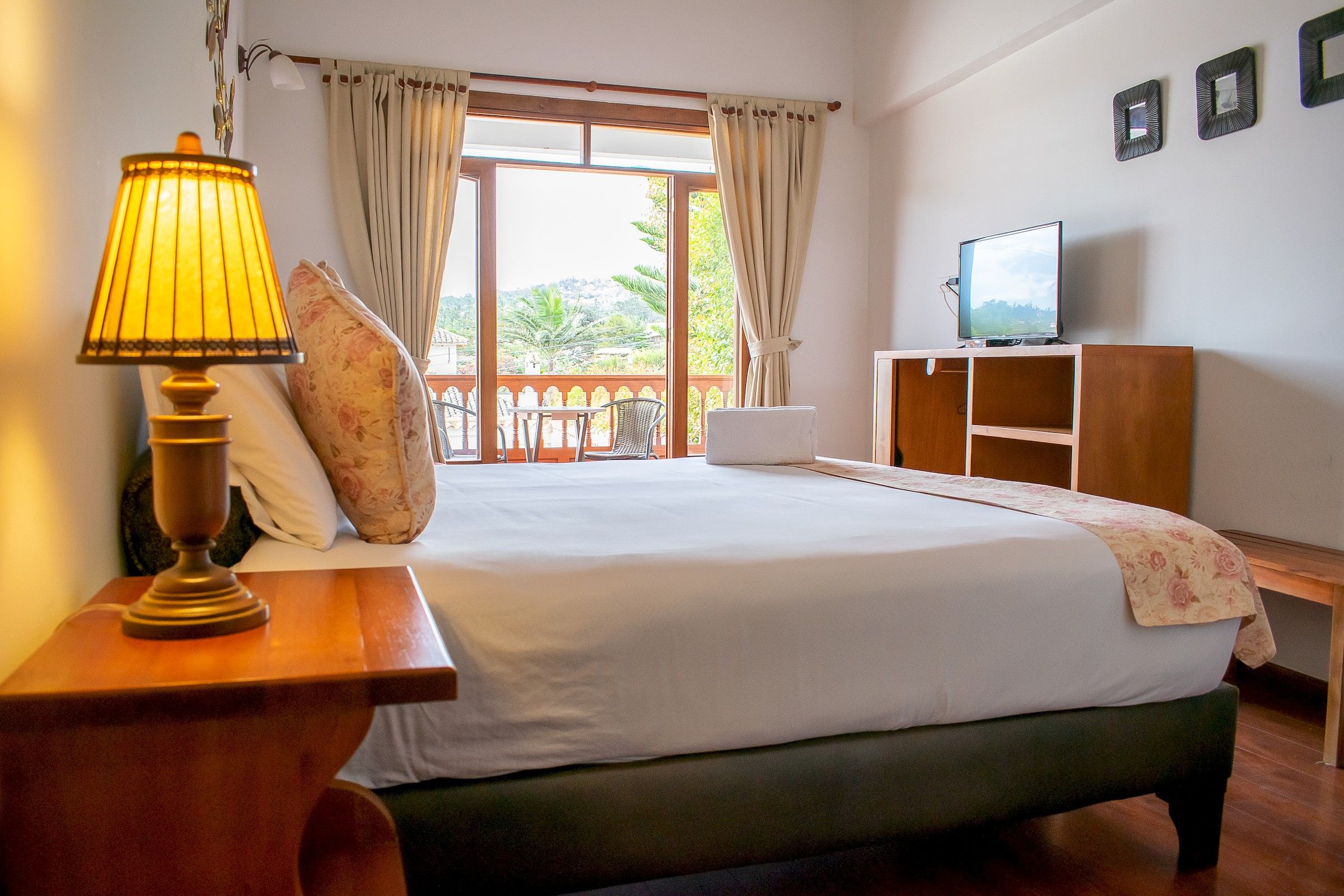 A hotel room with a bed, a television, a lamp, and a view of the outdoors.