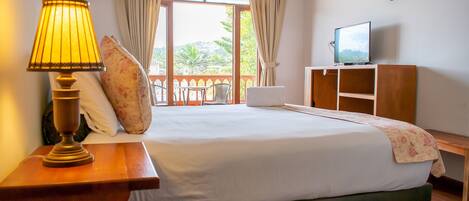 A hotel room with a bed, a television, a lamp, and a view of the outdoors.