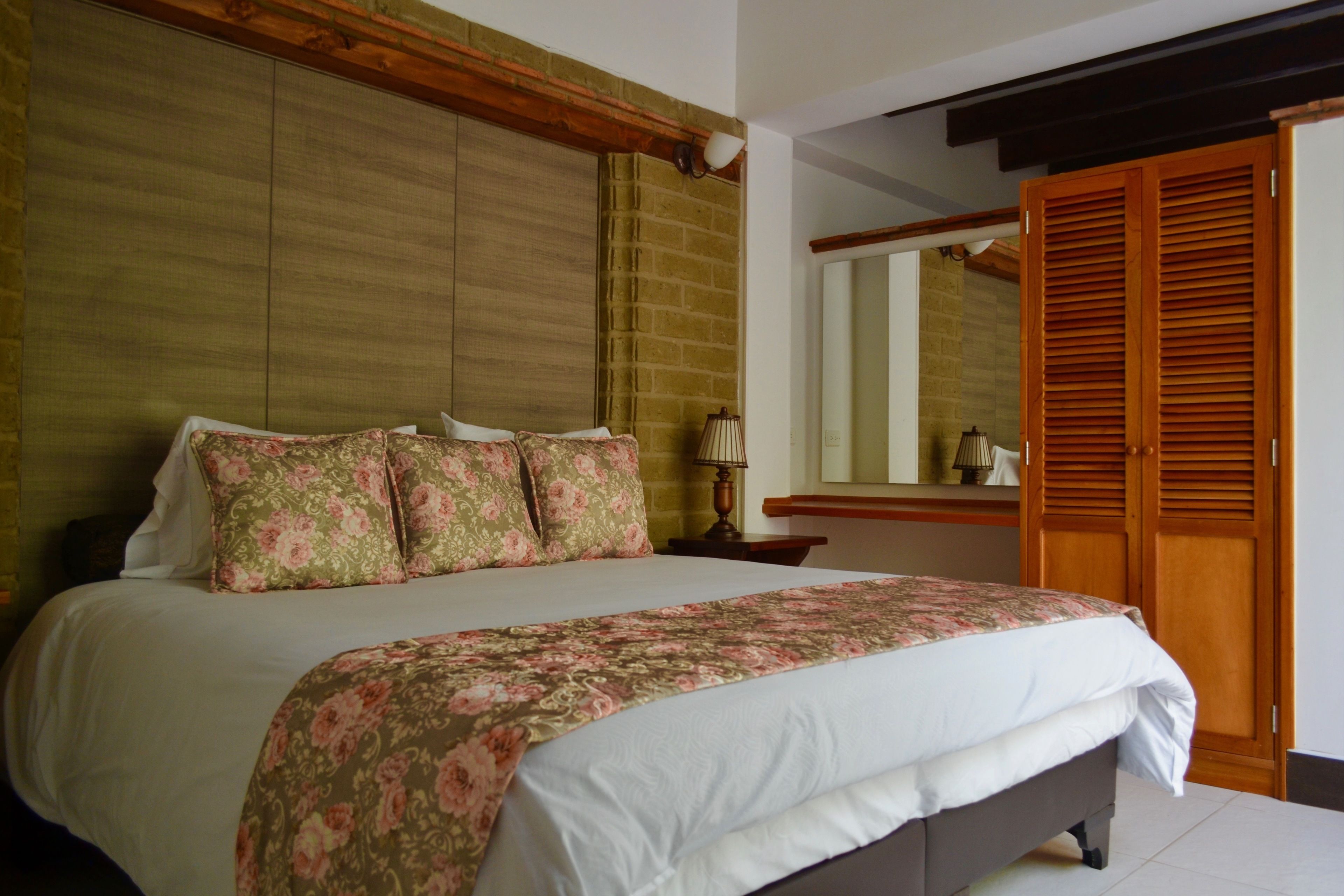 Une chambre à coucher avec un grand lit, une tête de lit en bois, une table de chevet, une lampe et une armoire avec un miroir.