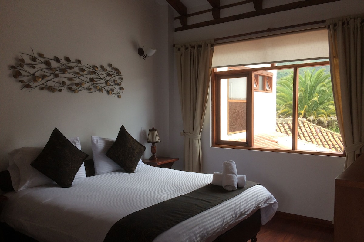 A neatly made bed with pillows and a lamp beside it, a window with curtains, and a wall decoration.