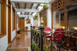 A corridor with wooden doors, potted plants, and a dining area with red chairs and a table.