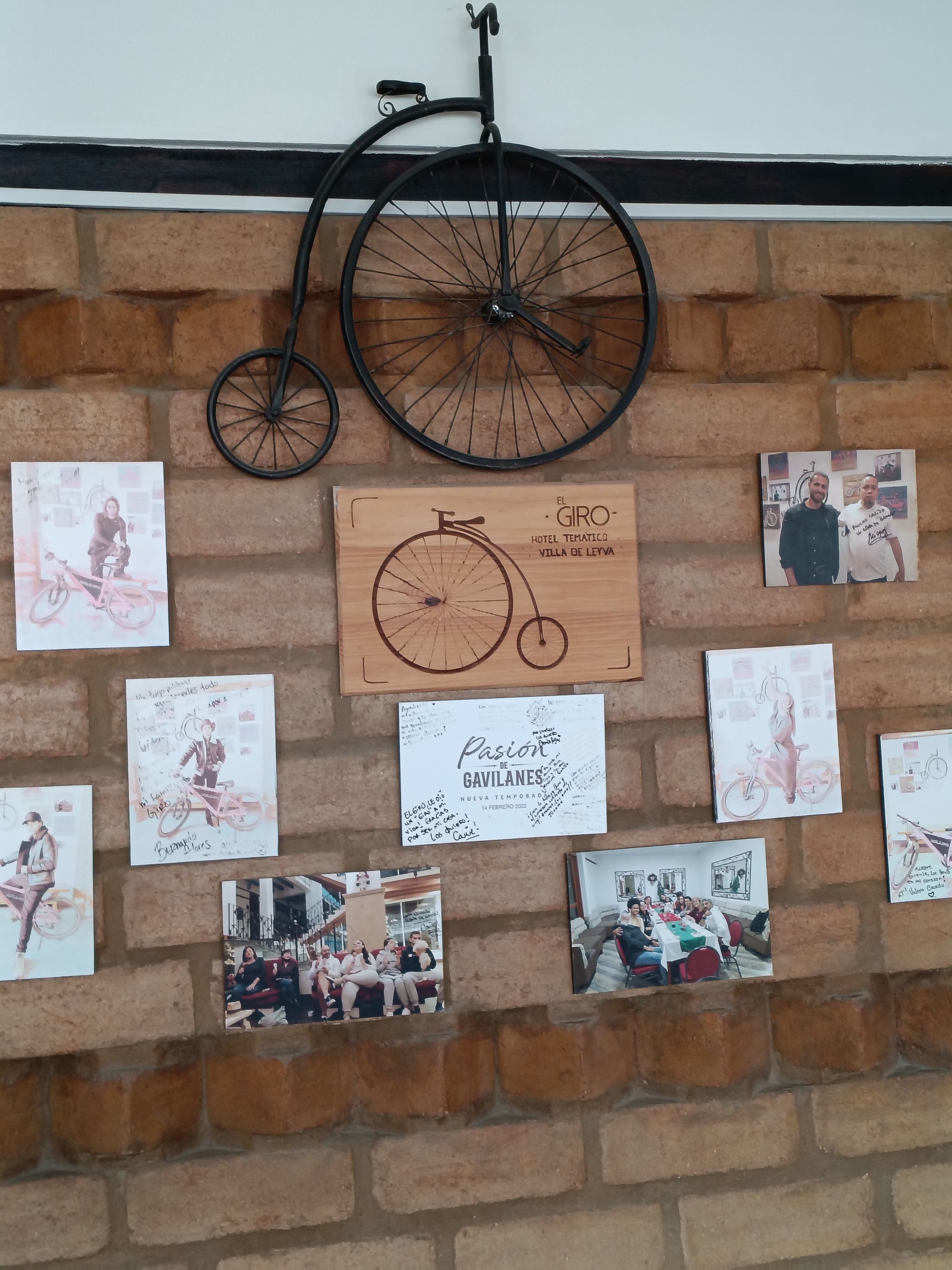 A brick wall with various framed photographs and a wooden signboard.