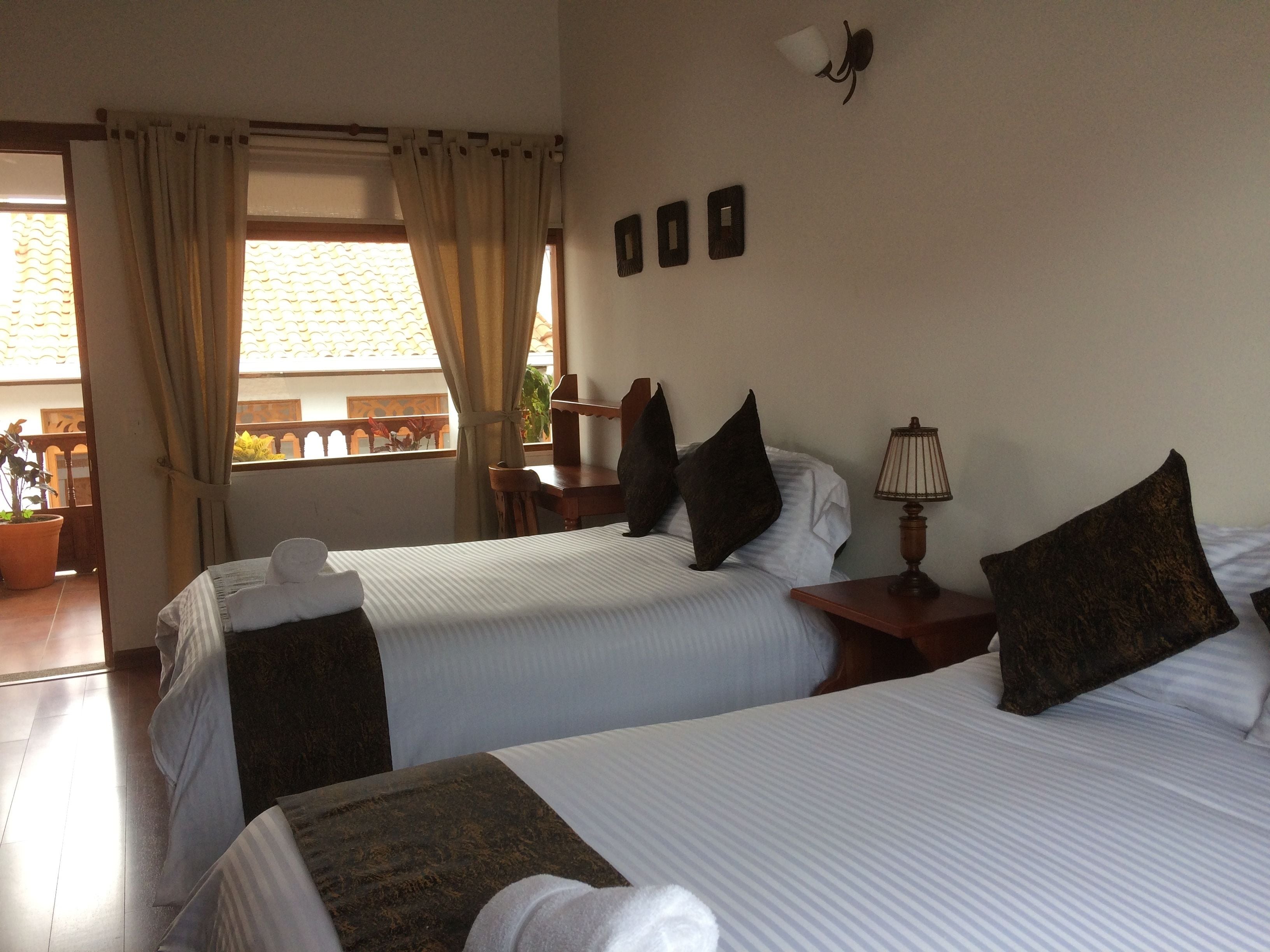 A hotel room with two beds, a nightstand, a lamp, and a view of the outside balcony.