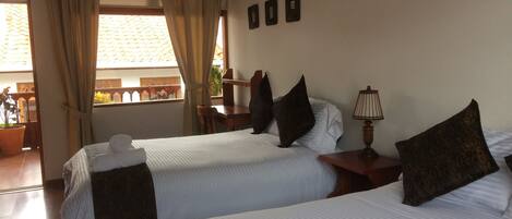 A hotel room with two beds, a nightstand, a lamp, and a view of the outside balcony.