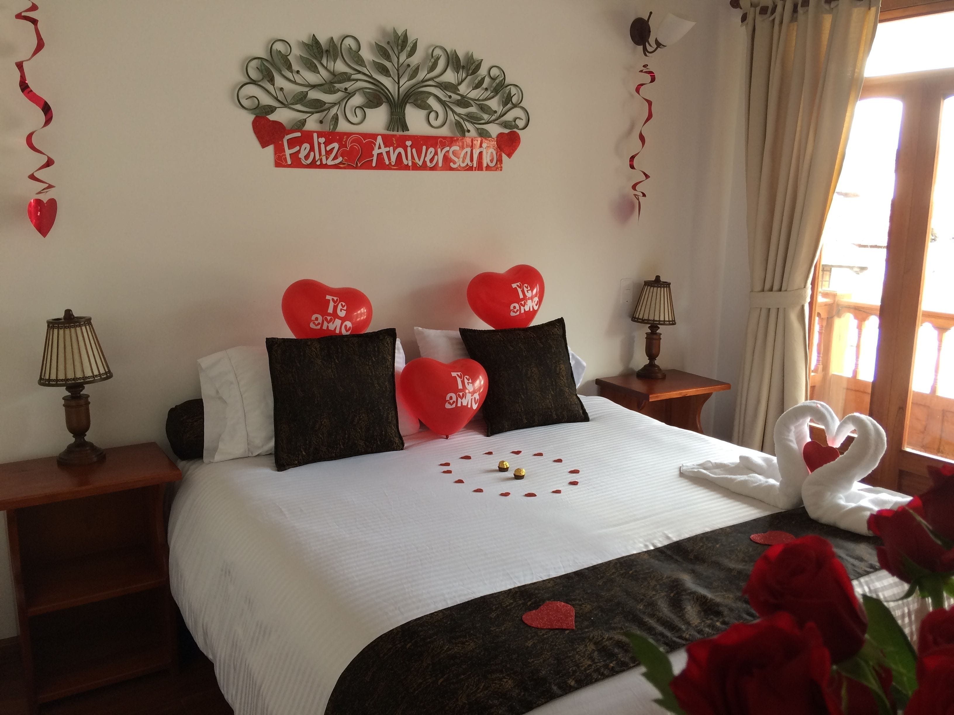 A neatly arranged bedroom with a bed, pillows, heart-shaped balloons, and a decorative wall piece.