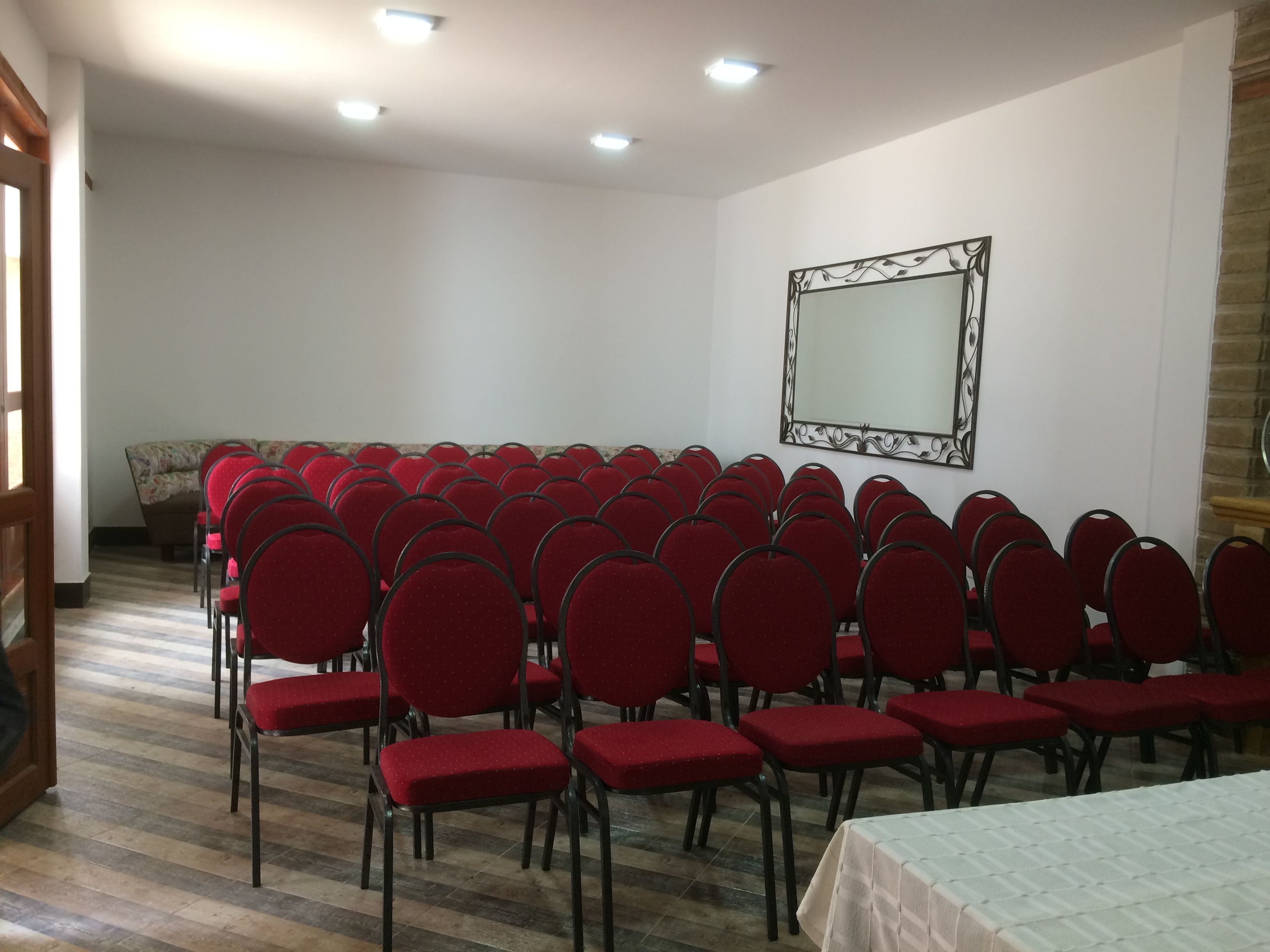 A conference room with rows of red chairs, a large mirror on the wall, and a wooden floor.
