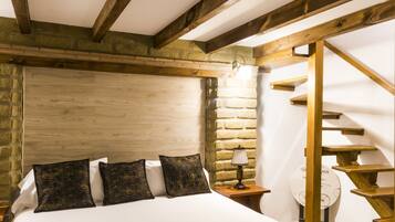 Un dormitorio con una cama grande, vigas de madera, una pared de piedra y una escalera.
