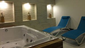 A modern bathroom with a large bathtub, two blue lounge chairs, and wall-mounted lights. - Hotel El Giro (Villa de Leyva)