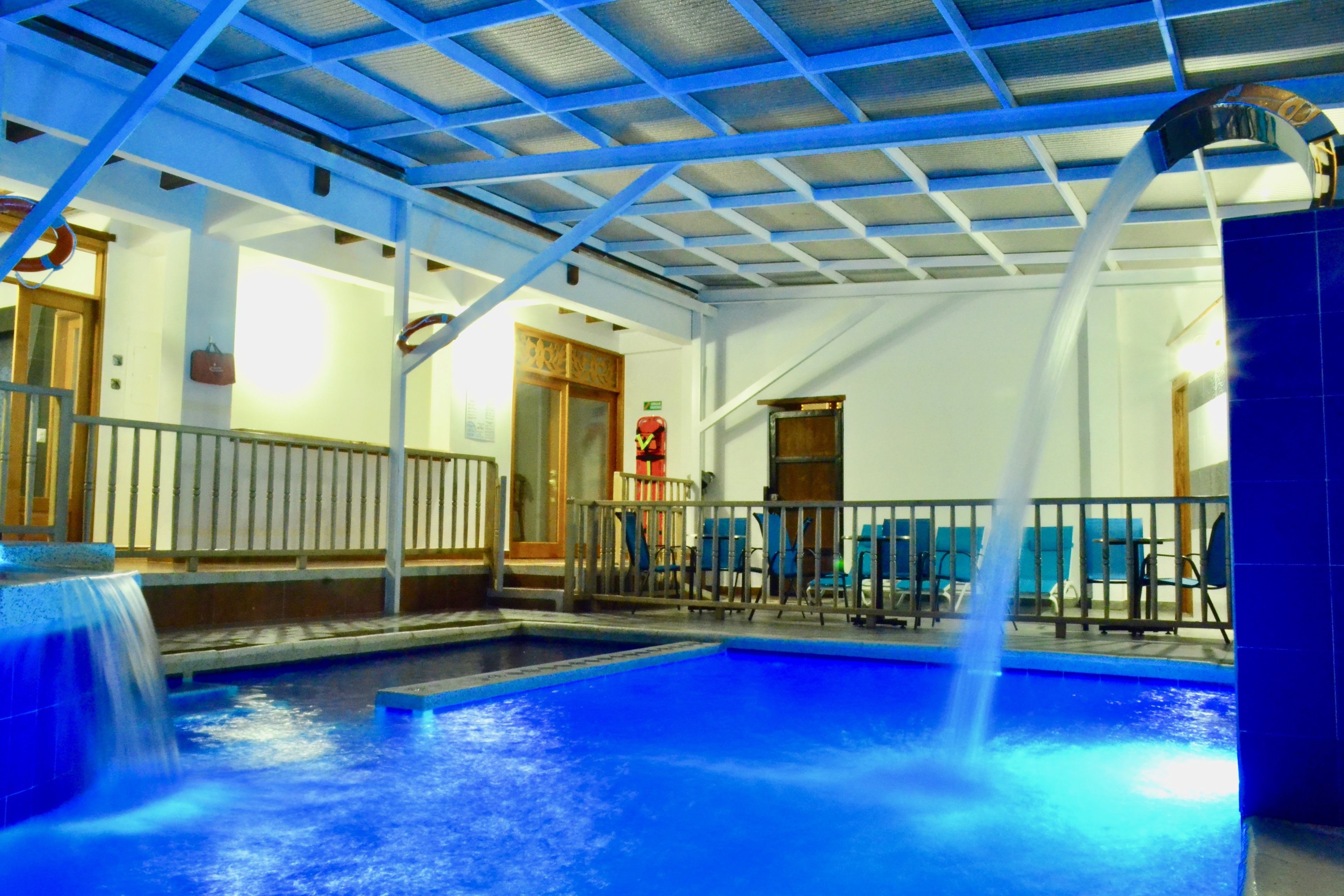 An indoor swimming pool with a blue-tiled floor, a water fountain, and a ceiling with a blue grid pattern.