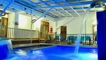 An indoor swimming pool with a blue-tiled floor, a water fountain, and a ceiling with a blue grid pattern.