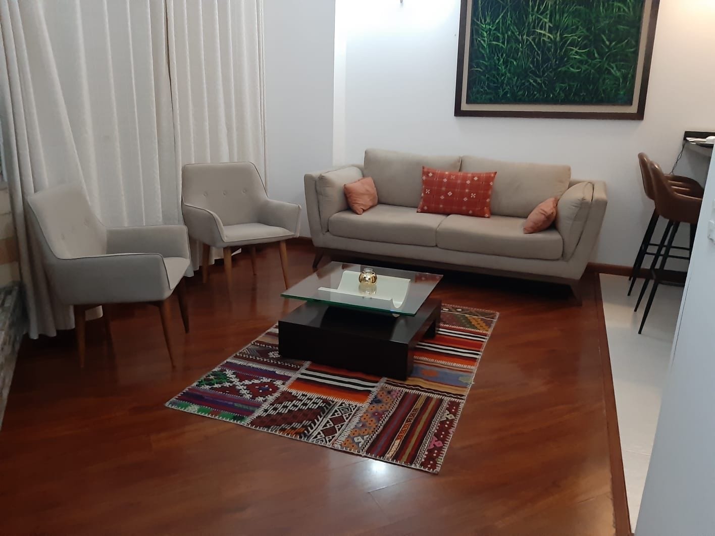 Ein Wohnzimmer mit einer Couch, zwei Sesseln, einem Couchtisch und einem gemusterten Teppich.
