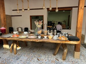 A breakfast buffet table with various food items and condiments, a coffee station, and a barista preparing drinks. - Hotel El Giro (Villa de Leyva)