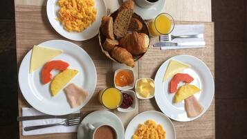 Una mesa de desayuno con huevos revueltos, tostadas y fruta, además de tazas de café y jugo de naranja.