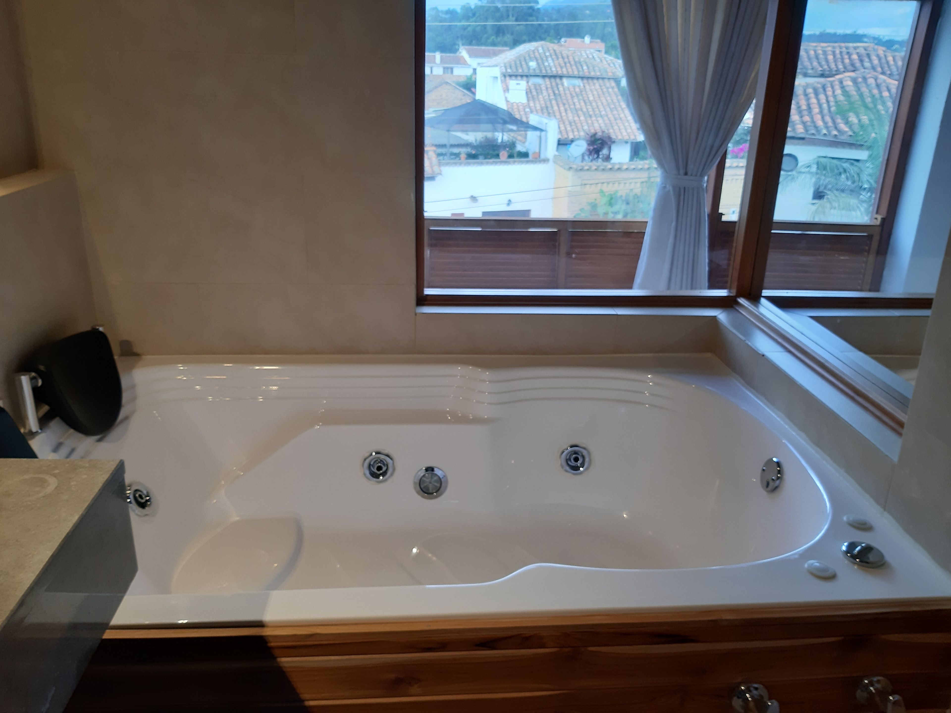 A bathroom with a large bathtub, wooden cabinetry, and a window with a view of houses.