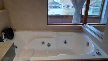 A bathroom with a large bathtub, wooden cabinetry, and a window with a view of houses.