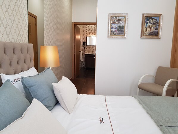 Una habitación de hotel con una cama, una silla, una lámpara y dos cuadros en la pared.