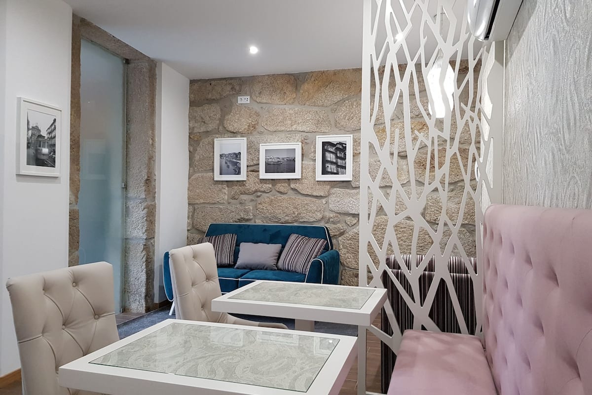 Una sala moderna con una pared de piedra, un sofá azul, un sillón beige y un sofá rosa. Hay tres cuadros enmarcados en la pared.