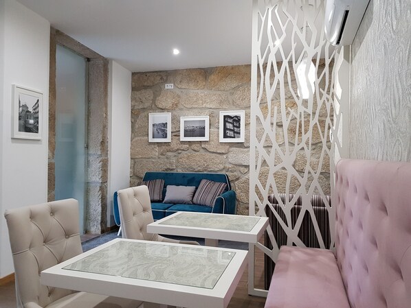 Una sala moderna con una pared de piedra, un sofá azul, un sillón beige y un sofá rosa. Hay tres cuadros enmarcados en la pared.