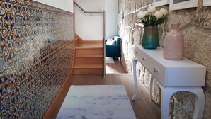 Un pasillo con baldosas estampadas, una escalera, un sofá azul y una consola blanca con objetos decorativos.