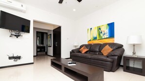 A modern living room with a dark leather sofa, a flat-screen TV mounted on the wall, and a colorful abstract painting above the sofa. - Heliko 104B by CocoBR (Playa del Carmen)