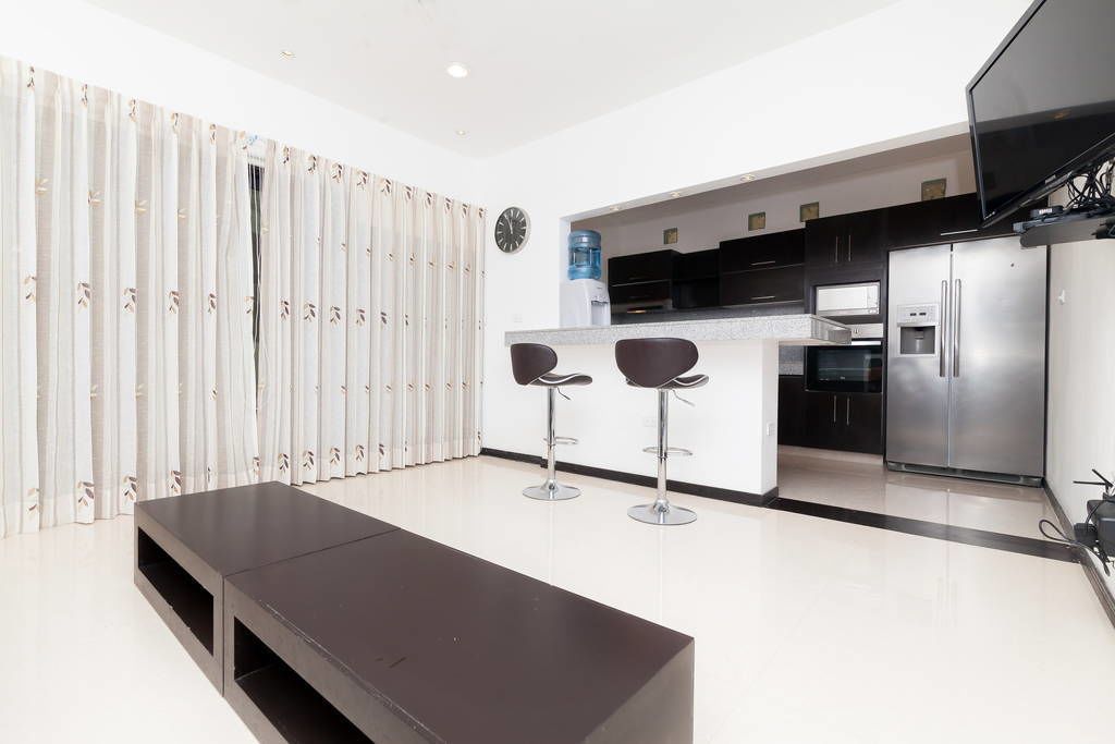 A modern kitchen with a central island, two bar stools, a large refrigerator, and a water dispenser.