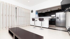 A modern kitchen with a central island, two bar stools, a large refrigerator, and a water dispenser. - Heliko 104B by CocoBR (Playa del Carmen)